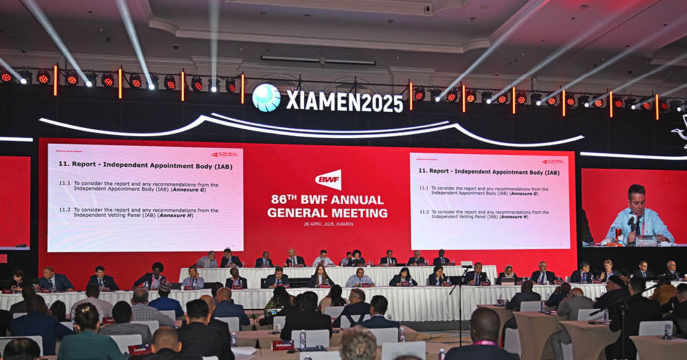 A large group of people are seated around a long table, engaged in a meeting. The attendees are wearing suits and ties, indicating a formal event. The meeting appears to be taking place in a conference room, with a large screen in the background. The attendees are focused on the screen, likely discussing or reviewing information displayed on it. AI generated content