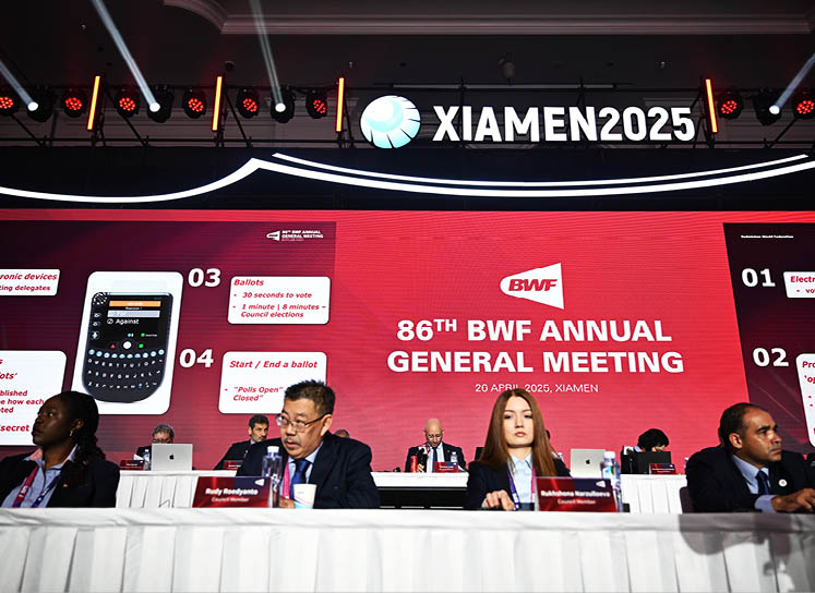 A group of people are sitting around a table, with some of them wearing ties. They are gathered for a meeting, with a sign on the wall indicating that it is the 88th BWF annual general meeting. There are several chairs, a laptop, and a cell phone on the table. AI generated content