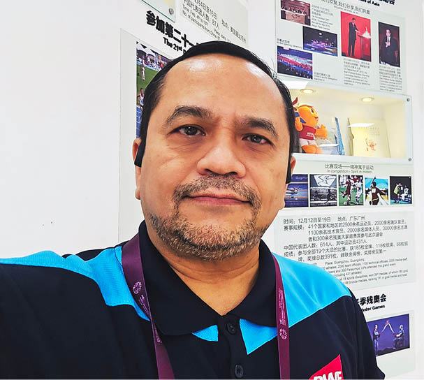 A man wearing a headset and a lanyard stands in front of a wall with many posters. AI generated content