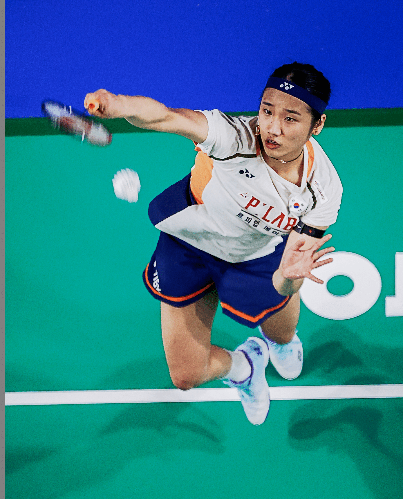 A tennis player in a white shirt and blue shorts is jumping to hit a tennis ball. AI generated content