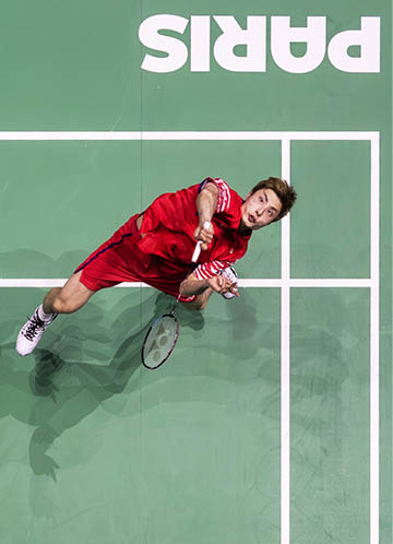 A man in a red shirt and red shorts is playing tennis on a court. He is swinging a tennis racket and appears to be jumping to hit the ball. AI generated content