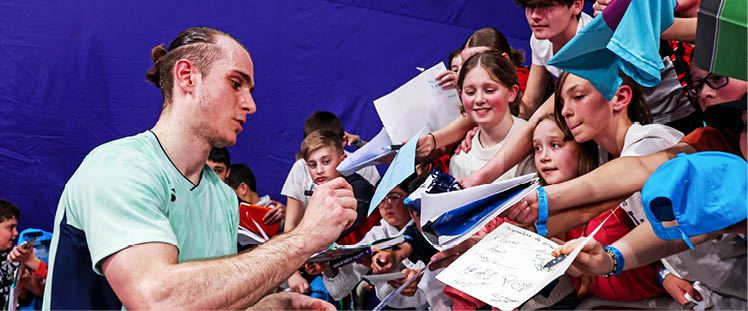 A man in a blue shirt is signing autographs for a group of people. AI generated content