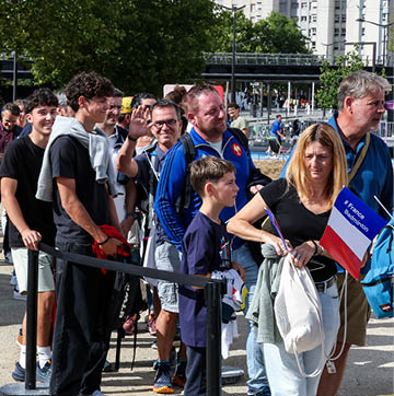 A group of people are standing in line, waiting to enter a building. They are holding their tickets and appear to be in a good mood. AI generated content