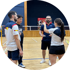 Four people are standing on a tennis court, holding tennis rackets. They are engaged in a conversation, possibly discussing a game or a strategy. The scene appears to be indoors, as there are no visible outdoor elements. AI generated content