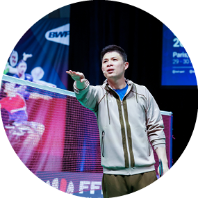 A man in a white jacket is standing on a tennis court in front of a large screen. AI generated content