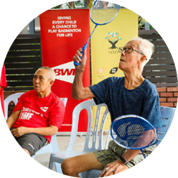 Three people are sitting on chairs, holding tennis rackets. They are watching a fourth person play tennis on a screen. AI generated content