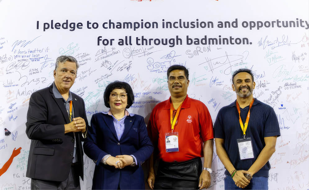 Four people pose for a photo in front of a sign that says “I pledge to champion inclusion and opportunity for all through badminton." AI generated content