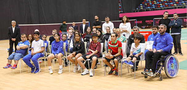 A group of people, including children, are sitting on chairs on a tennis court. They are posing for a picture. AI generated content