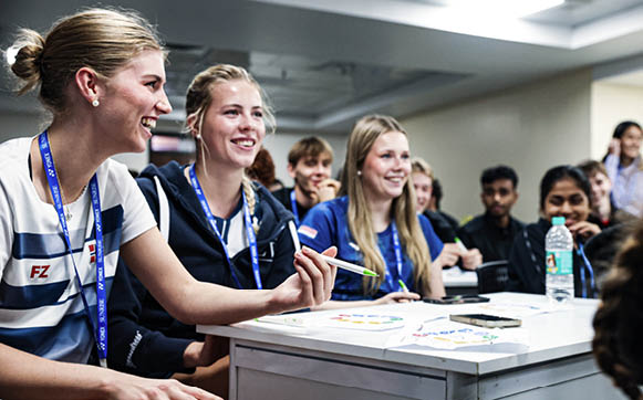 A group of people are sitting around a table, smiling and laughing. They are wearing lanyards and appear to be enjoying a social event. AI generated content