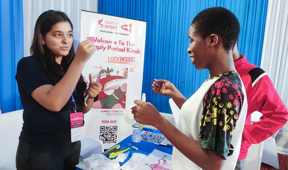Two women are standing at a table, one of them holding a cell phone. They are engaged in a conversation, possibly discussing the content on the phone screen. AI generated content